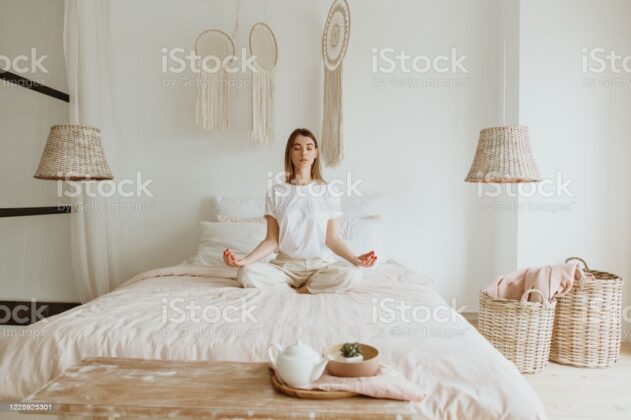 Beautiful young woman practicing meditation on the bed.