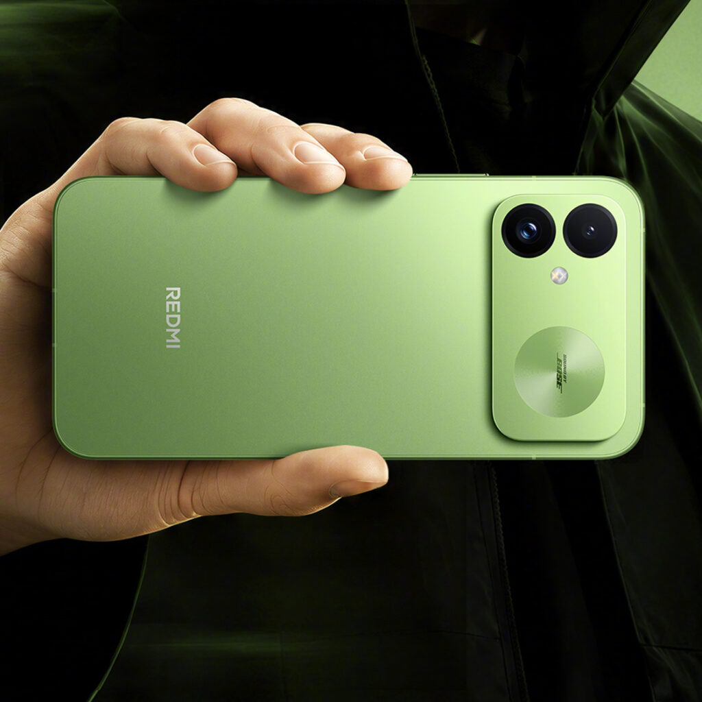 A hand holds a light green Redmi K100 smartphone featuring a dual-camera module.