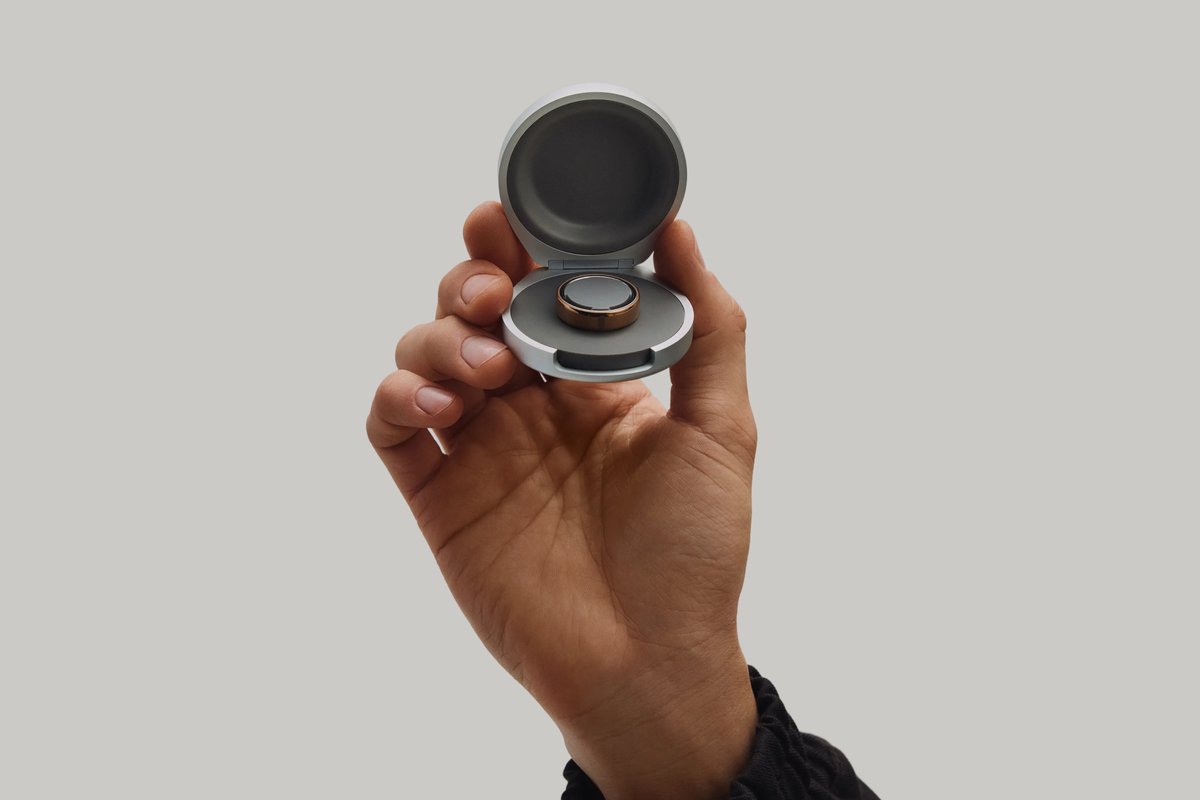 Hand holding the open Oura Ring 5 Charging Case with a ring seated on the charger